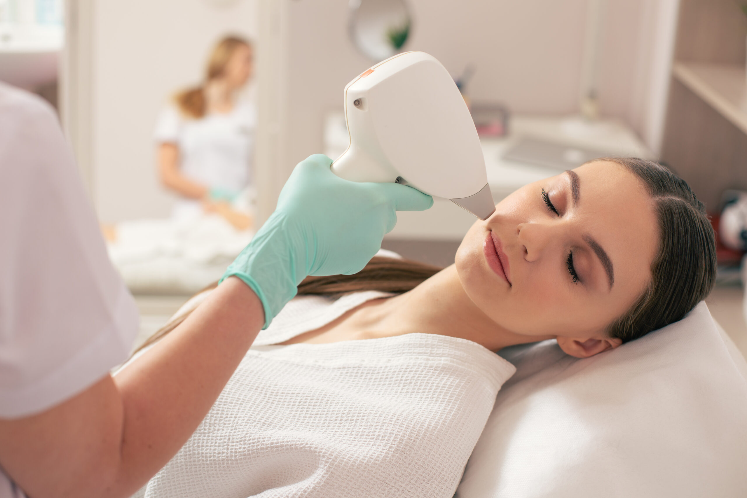 Close up of young woman visiting professional cosmetician and having modern laser hair removal procedure on her face