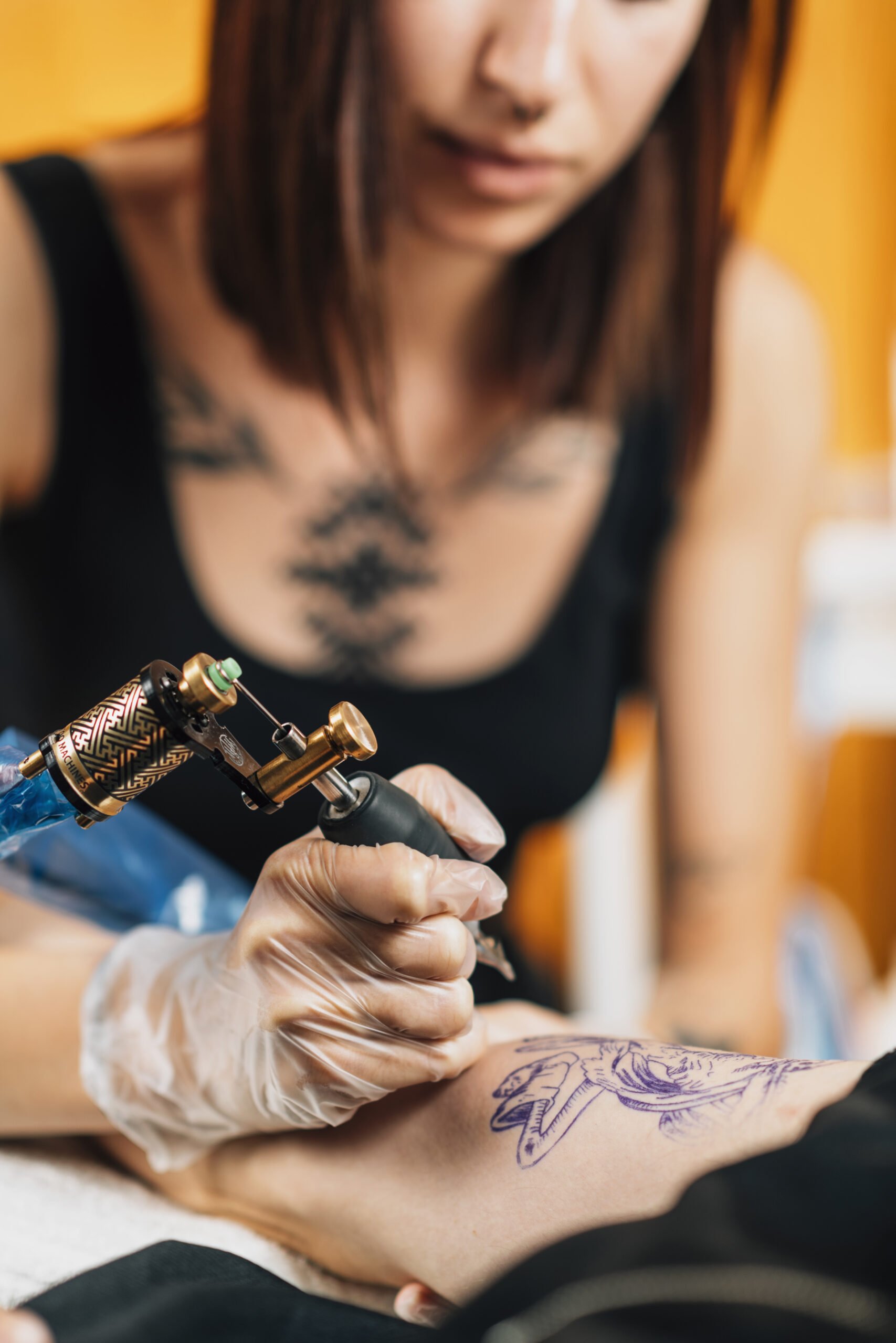 Female tattoo artist tattooing man’s arm in studio